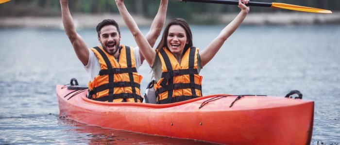 Happy young couple in sea vests is smiling while sailing a kayak